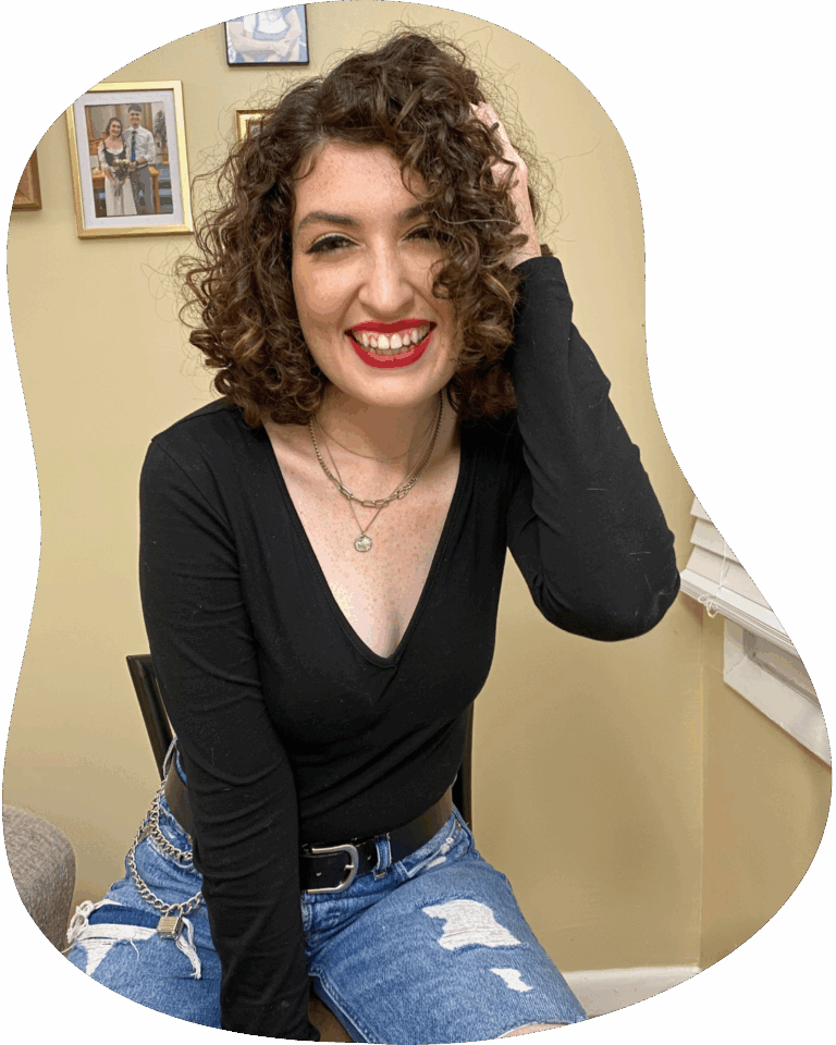 Kat, a white woman with curly brown hair and red lipstick, is smiling at the camera