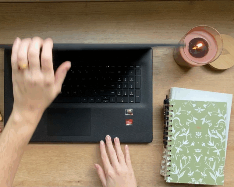 Closing laptop on wood desk with a green notebook planner and lit cinnamon candle